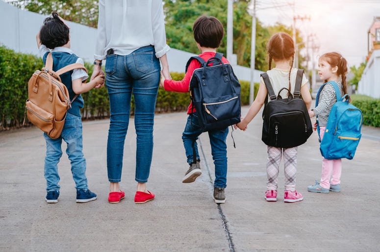 (champlifezy@gmail.com/ iStock/ Getty Images Plus) Motherl and kids holding hands going back to school with backback.