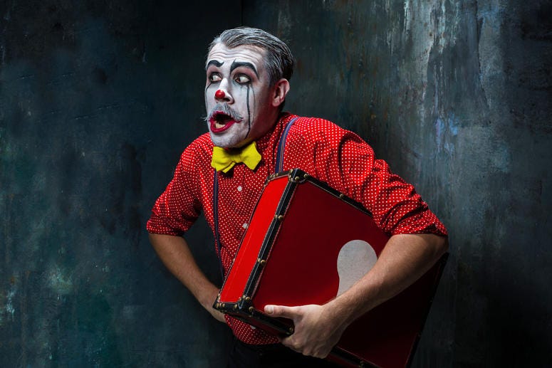(0master1305/ iStock/ Getty Images Plus) Terrible clown with suitcase and a dark background