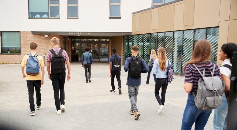 Rear View Of High School Students Walking Into College Building Together