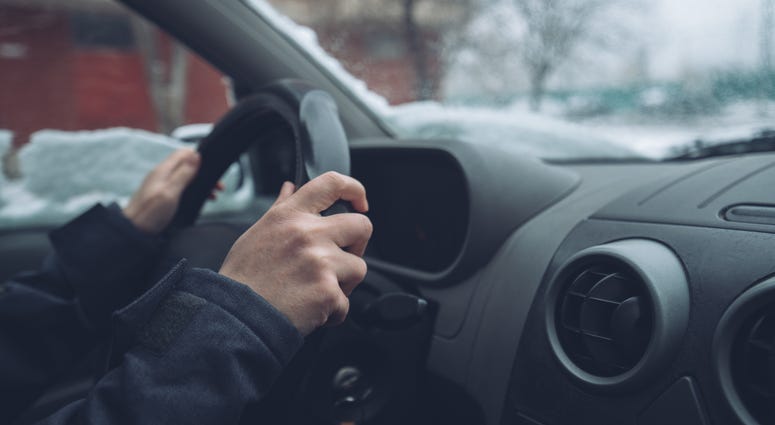 Photograph of a driver's hands on the steering wheel of a car, with snow on the windshield