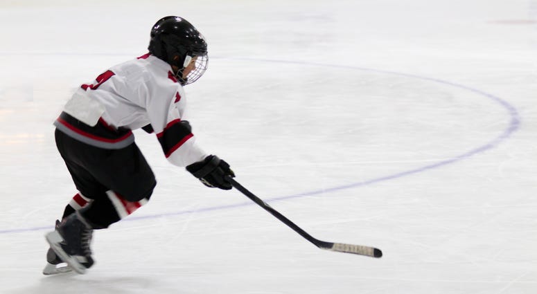 A little boy in a full hockey uniform skates and handles a puck with his stick