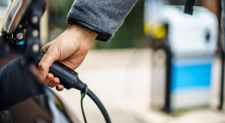 Close-up image of person's hand attaching charger cord to electric vehicle