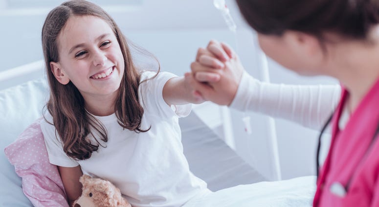 Nurse holding smiling girls hand in hospital bed