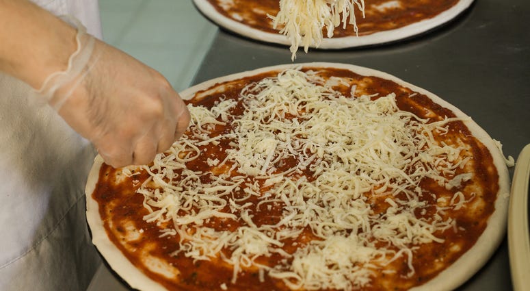 a man makes a pizza pie, sprinkling shredded cheese