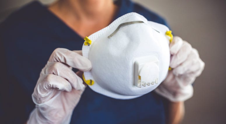 a medical worker wearing gloves holds an N95 style facemask