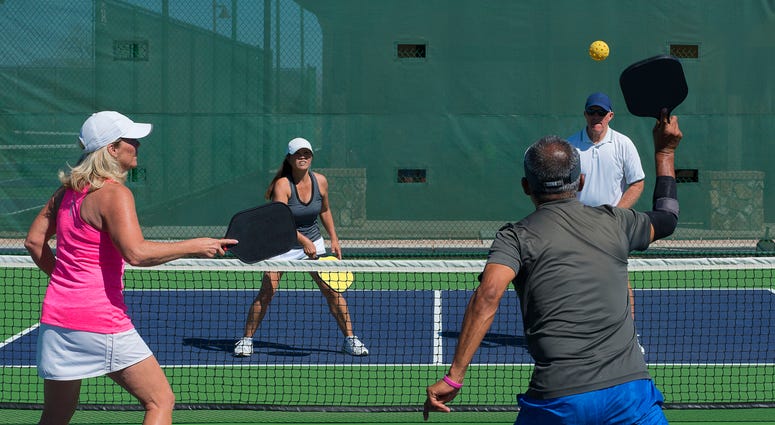 four people play pickleball, a game like tennis with a wiffle ball