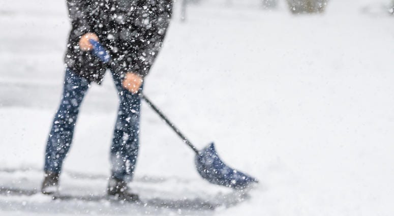 Man in winter coat shoveling driveway during heavy snowstorm.