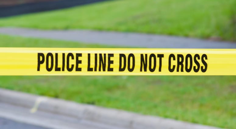 Yellow crime scene tape in a suburban neighborhood reads, "Do not cross."