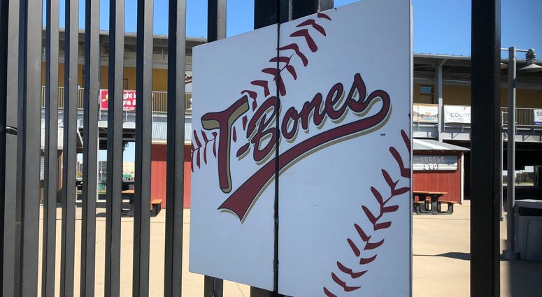 A sign reading "T-Bones" hangs on the gate of the baseball stadium