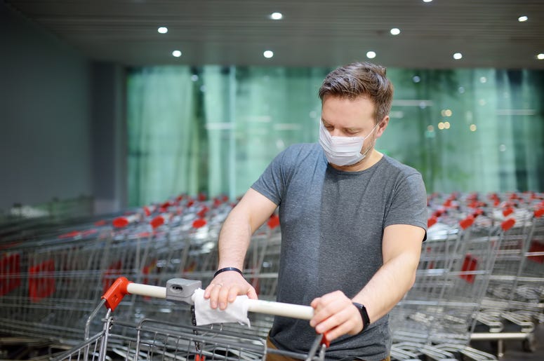 Man in face mask disinfects grocery shopping cart Man in face mask disinfects grocery shopping cart