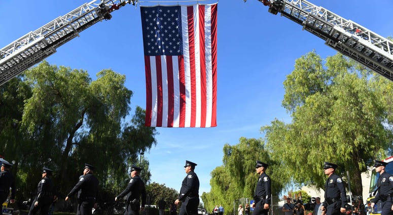 Police officers walk under a large American flag on their way to the funeral Police officers walk under a large American flag on their way to the funeral