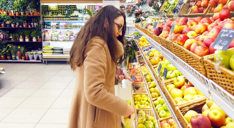 Woman selecting fresh red apples in grocery store produce department and putting it in plastic bag.