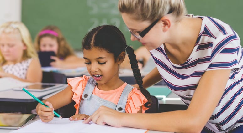 Teacher helping kids with their homework in classroom at school
