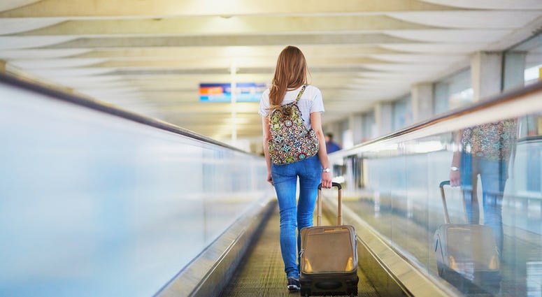 Airport Traveler Tourist girl with backpack and carry on luggage in international airport, on travelator