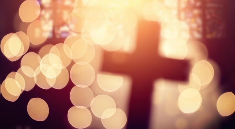Abstract defocussed cross silhouette in church interior against stained glass window concept for religion and prayer