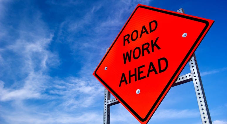 road work, construction Image of a bright orange road work ahead sign against a blue sky with light clouds
