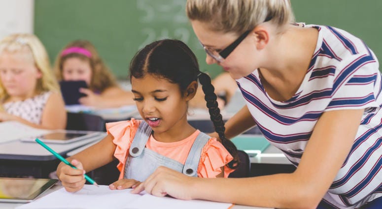 Teacher helping kids with their homework in classroom at school