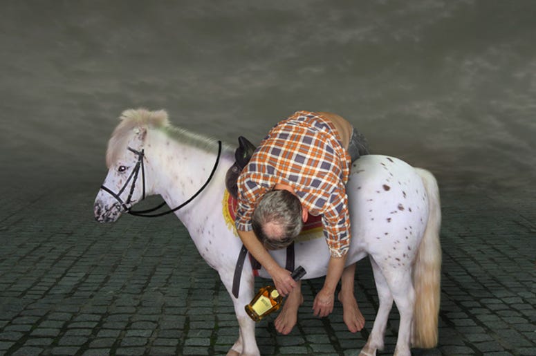 Borracho De Dallas Arrestado Por Andar A Caballo En Carretera The drunk man with a bottle of rum is lying across the horse saddle.