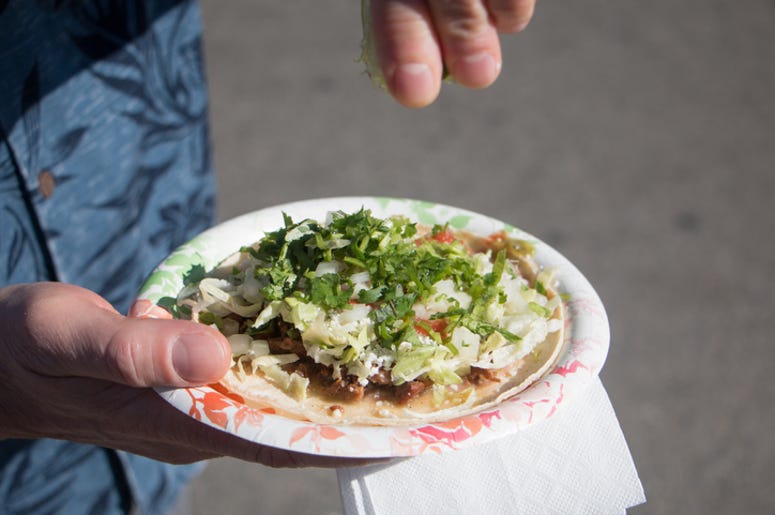 Señora Come Tacos Con Tijeras A lime is being squeezed onto a carne asada taco on a paper plate.