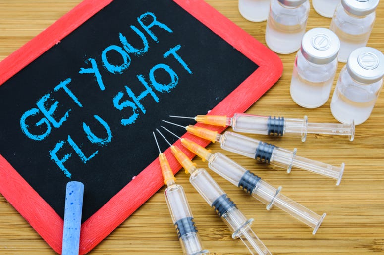 Fort Worth Quiere Que Ya Te Vacunes Contra La Flu Reminder to Get Your Flu shot written on chalkboard with vaccine in syringes and vials