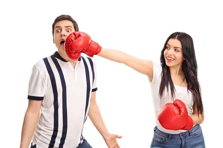 Novia Noquea A su Novio Jugando Al Box Cheerful woman punching her boyfriend with boxing gloves isolated on white background
