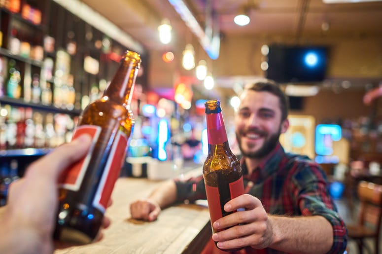 Gente De Dallas Gastó En Pisto Más De $80 Millones De Dólares Portrait of happy bearded man clinking beer bottles with friends while having fun in pub sitting at bar counter, focus on foreground
