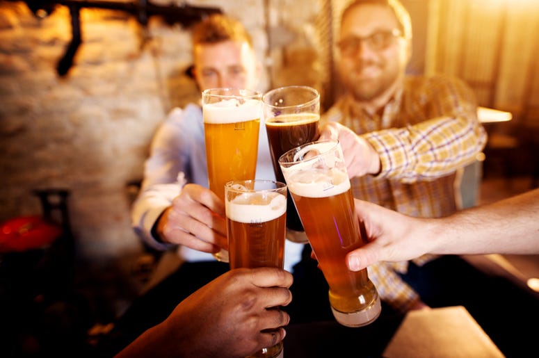 Gente De Dallas Gastó 76 Millones De Dólares En Bebidas Alcohólicas A group of young men clinking glasses with a beer in the sunny pub.