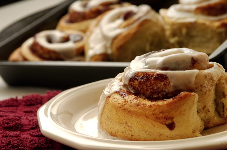 Cinnamon roll on a plate with a pan full of more cinnamon rolls Cinnamon roll on a plate with a pan full of more cinnamon rolls