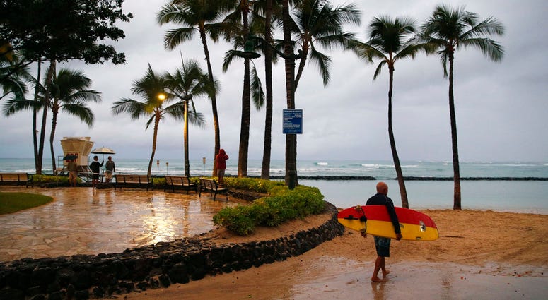 A surfer walks along Waikiki Beach in a light rain from Tropical Storm Lane, Saturday, Aug. 25, 2018, in Honolulu