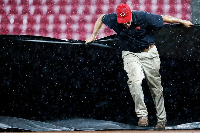 A member of the grounds crew helps pull a tarp onto the infield during a rain delay in the third inning o