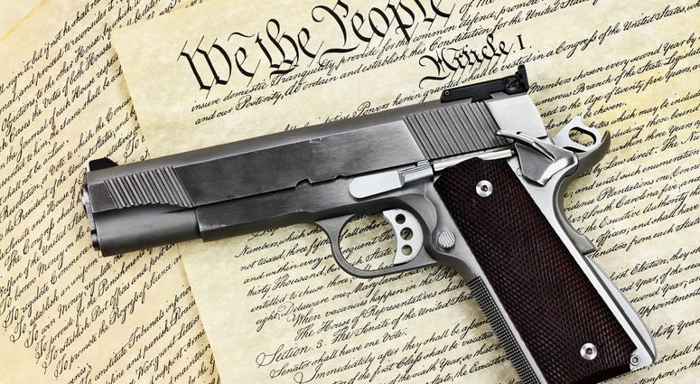Handgun lying over a copy of the United States constitution with the words "We the People" visible.