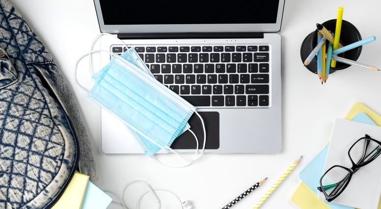 Modern laptop with backpack, stationery and mask