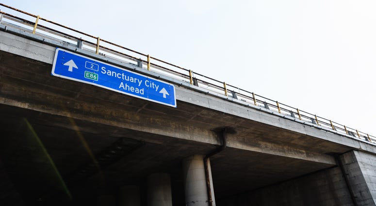 A blue traffic road sign with the message "Sanctuary City Ahead"