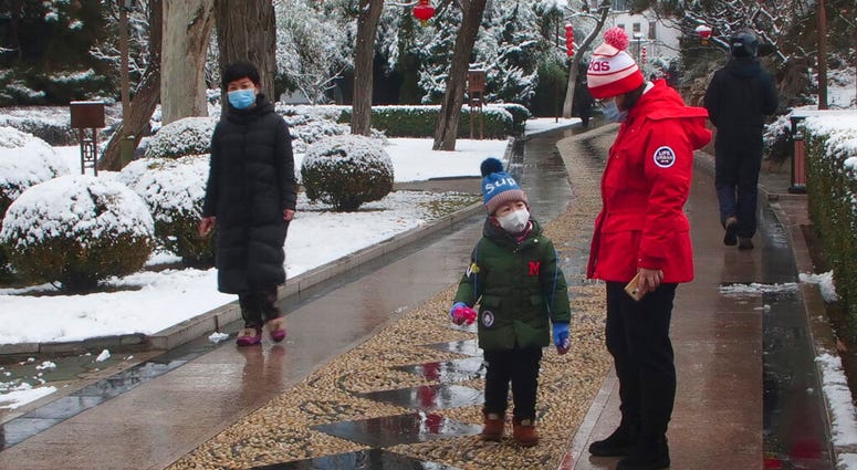People wear face masks as they walk in public park on a snowy day in Beijing, Sunday, Feb. 2, 2020. T