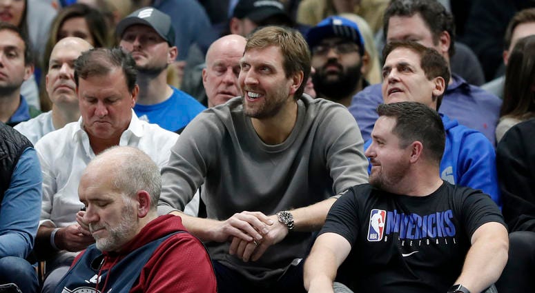 Former player Dirk Nowitzki, center, and team owner Mark Cuban, right, watch play between the Cleveland Cavaliers and Dallas Mavericks in the second half of an NBA basketball game in Dallas, Friday, Nov. 22, 2019.