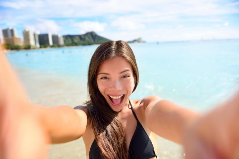 Selfie fun woman taking picture at beach vacation. Summer holiday girl happy at smartphone camera taking self-portrait on her Hawaiian travel vacations in Waikiki, Honolulu city, Oahu, Hawaii, USA.