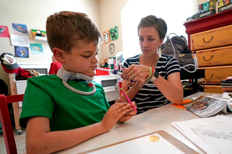 Rachel Scott, right, helps suction the mouth of her son, Braden, in Tomball, Texas on Friday, March 29, 2019. He was 7 on July 4, 2016, when he uncharacteristically decided he didn’t want to go swimming. He had trouble swallowing and felt tired and weak.