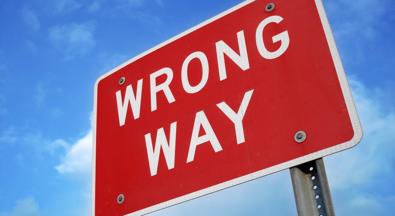 Wrong way sign at angle against blue sky with clouds.