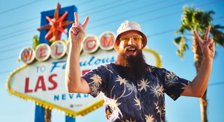 retro tourist making peace sign in front of welcome to las vegas sign during the day