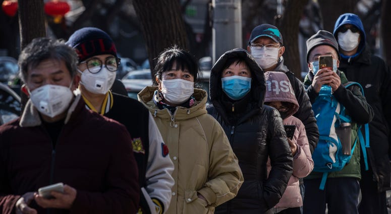 Chinese customers wear protective masks as they line up single file to buy dumplings at a popular local shop on February 16, 2020 in Beijing, China