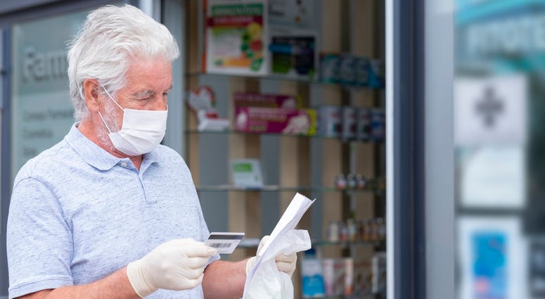 Elderly man with mask and protective gloves leaves the chemist's shop with medicines and instructions.