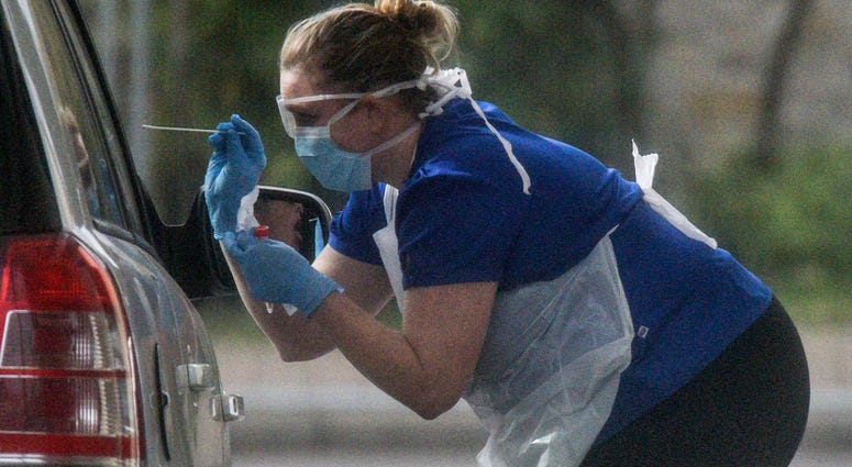 A nurse is seen swabbing the occupants of a car at a drive through COVID-19 testing station