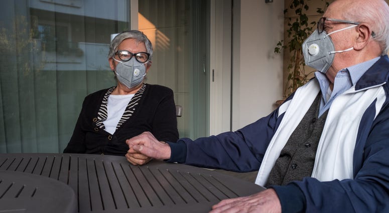 An elderly couple wearing a protective mask and holding hands