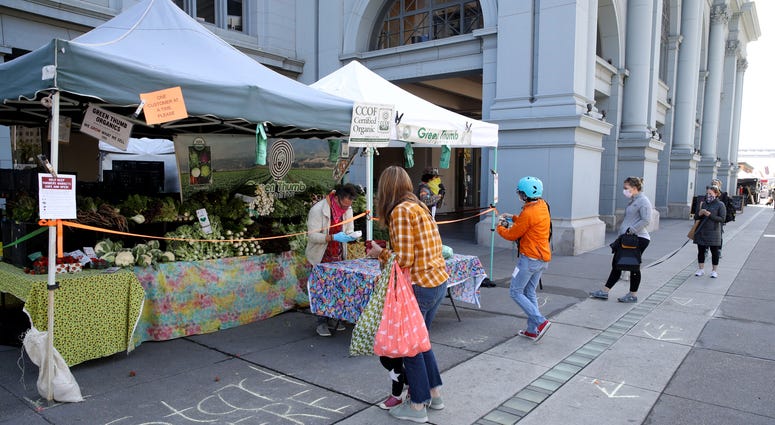 People practice social distancing as they wait in line to purchase produce from a vendor during the Ferry Plaza Farmers Market on April 21, 2020 in San Francisco, California