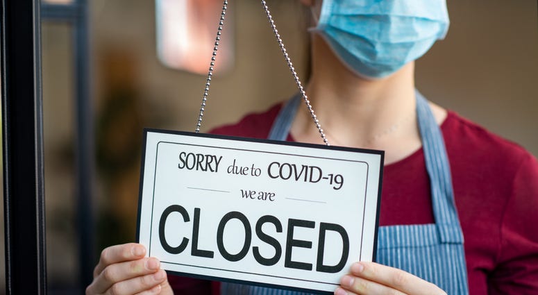 Businesswoman closing her business activity due to covid-19 lockdown. Owner with surgical mask close the doors of her store due to quarantine coronavirus damage.
