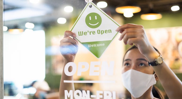 Business owner Asian woman wear protective face mask ppe hanging open sign at her restaurant / café, open again after lock down due to outbreak of coronavirus covid-19