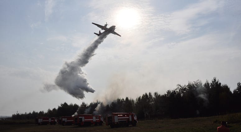 Helicopter drops water on a brush fire as a firefighter watches on