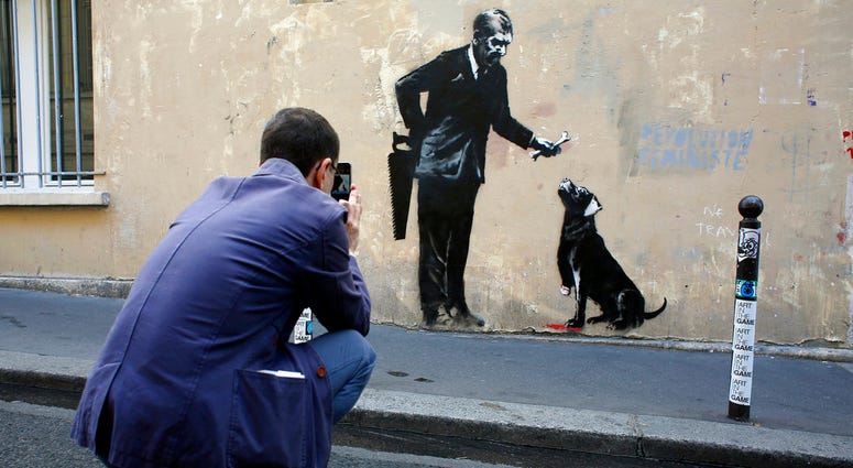A man takes a picture of a graffiti believed to be attributed to street artist Banksy, in Paris. A man takes a picture of a graffiti believed to be attributed to street artist Banksy, in Paris.