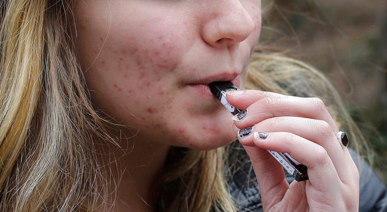 In this April 11, 2018, file photo, an unidentified 15-year-old high school student uses a vaping device near the school's campus in Cambridge, Mass. An unidentified 15-year-old high school student uses a vaping device.