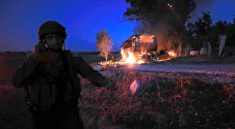 An Israeli soldier stands near a burning bus after it was hit by a mortar shell fired from Gaza near the Israel Gaza border, Monday, Nov. 12, 2018. An Israeli soldier stands near a burning bus after it was hit by a mortar shell fired from Gaza near the Israel Gaza border, Monday, Nov. 12, 2018.